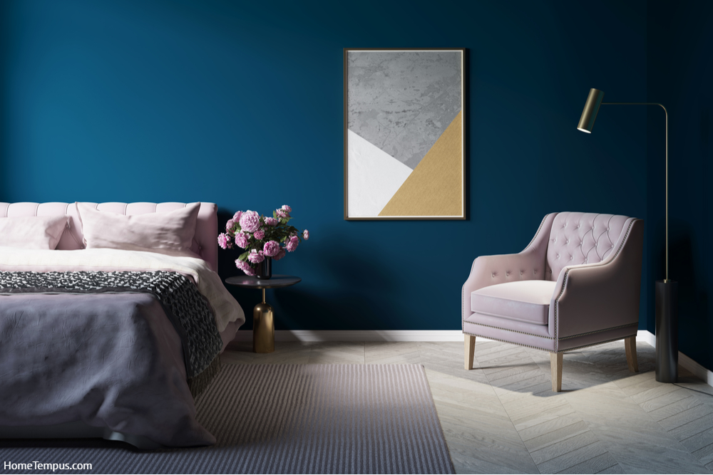 A cozy dark room with a lamp next to a pink armchair, a vertical poster on a dark blue wall, peonies on a nightstand next to a bed with pink linen. Front view -  Pink Two Colour Combination for Bedroom Walls