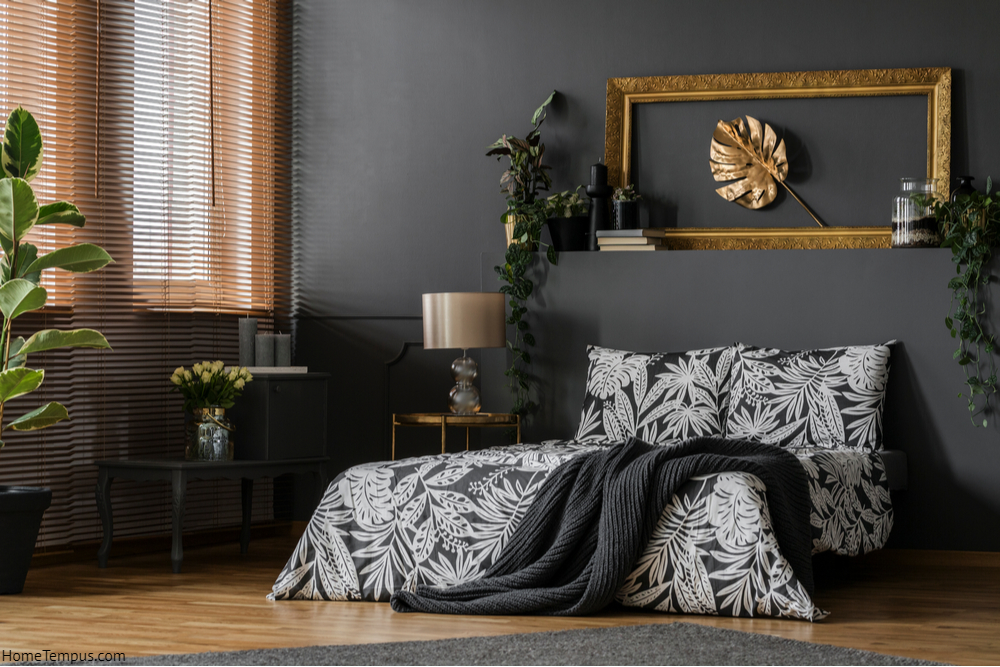 Glass lamp placed on a gold end table standing by the king-size bed in dark grey bedroom interior with windows and green plants - Ash and Gold Bedroom Walls Colour Combination
