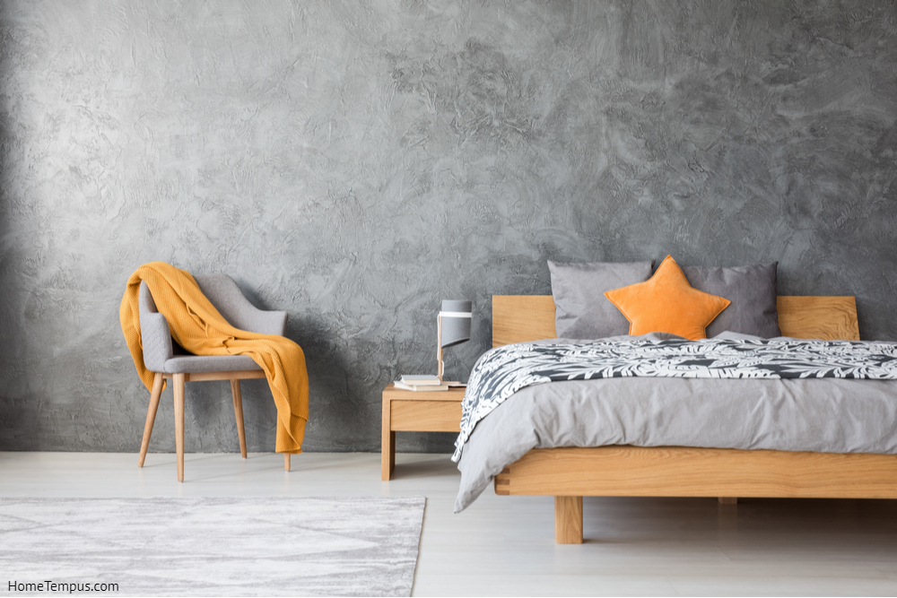 Ash grey and mandarin orange bedroom - Orange star pillow on wooden bed against concrete wall with copy space in grey bedroom with chair