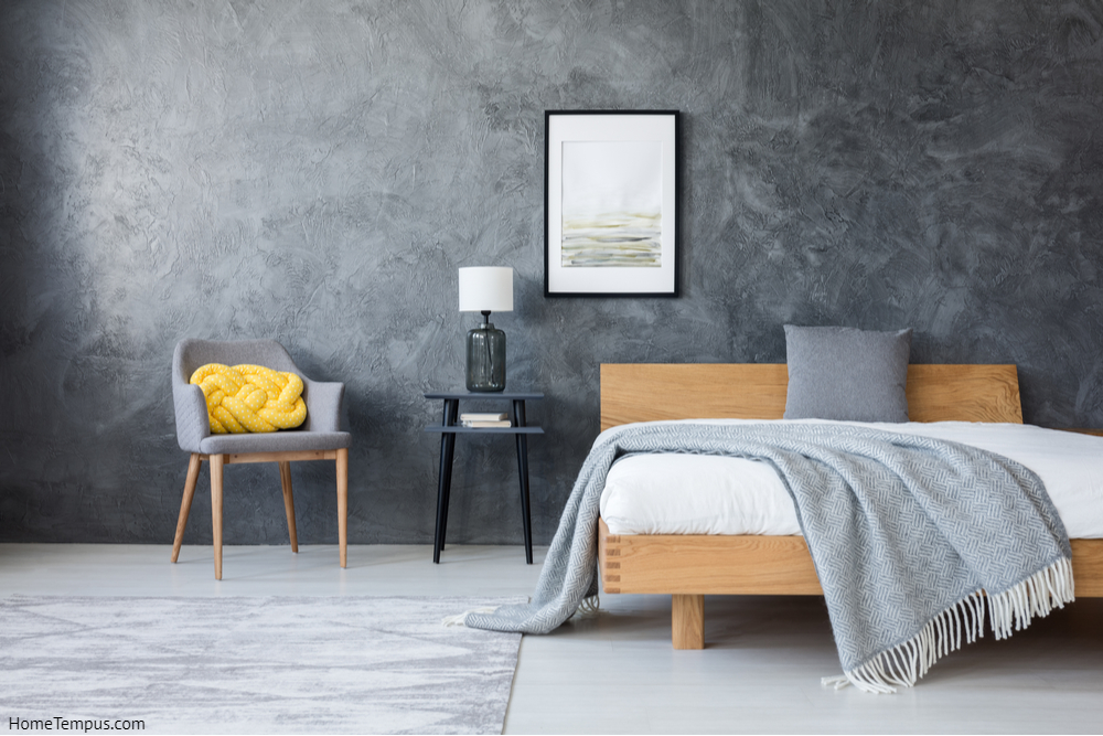 Two Colour Combination for Bedroom Walls Gray - Poster on concrete wall above stool with lamp and wooden bed in dark bedroom with yellow pillow on a chair - 
