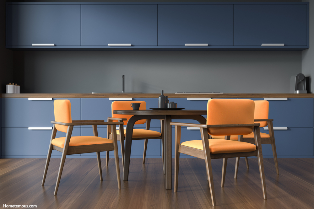 Blue and gray kitchen cabinets. Interior with orange chairs surrounding dining table and dark wood flooring. Concept of modern house design.