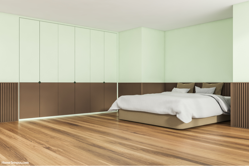 Interior design of trendy bedroom in soft shade of green. Wood floor, basement ledge, comfortable bed and creative wardrobe.