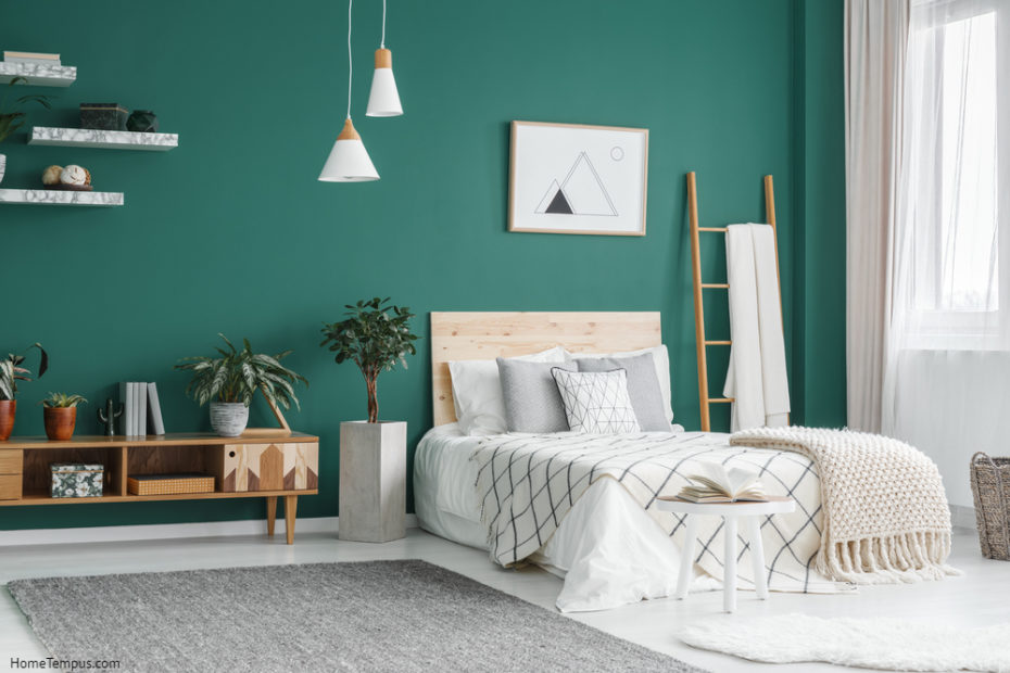 Bed between ladder and plant in green boho bedroom interior with grey carpet under lamps