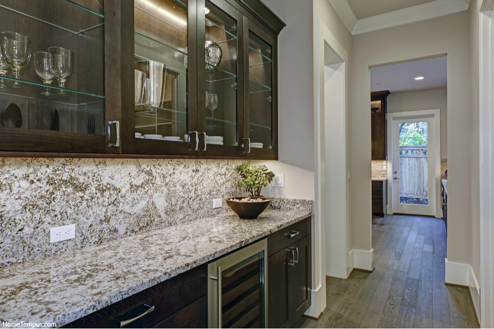 Brown wet bar boasts glass front cabinets paired with gray and white granite countertops 