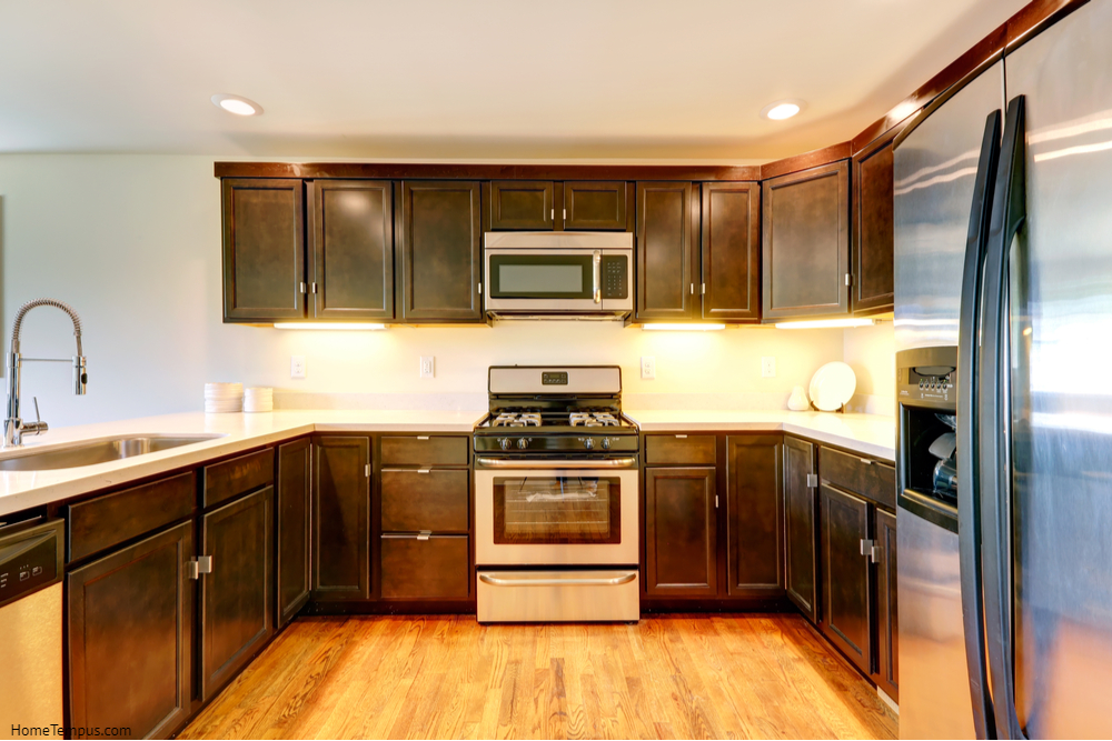 Dark brown kitchen room with steel appliances. Yellow wooden floor with dark cabinets
