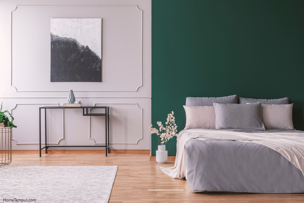 Dark green wall with copy space in stylish scandinavian bedroom interior with metal table, black and white abstract painting on the grey wall and carpet on wooden floor,