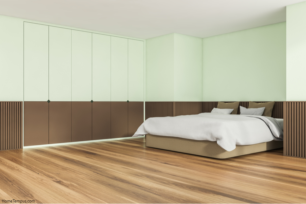 Interior design of trendy bedroom in soft shade of green. Wood floor, basement ledge, comfortable bed and creative wardrobe. Corner view. A concept of a modern apartment.