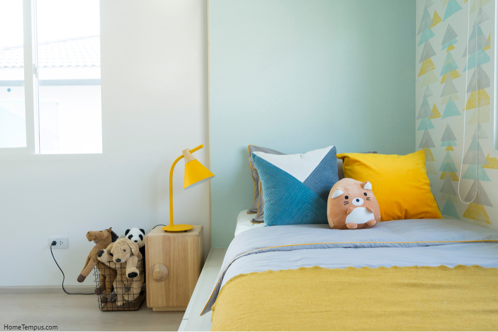 Kid bedroom in blue and yellow tone pillow with many doll on bed.