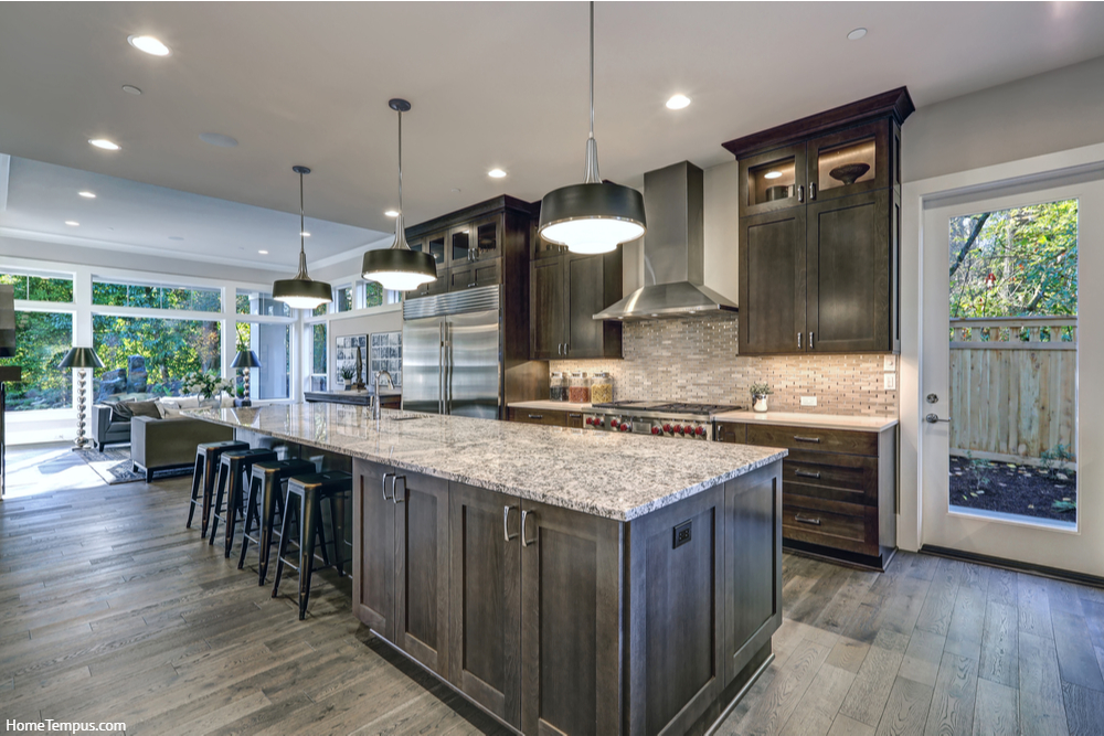 Modern kitchen with brown kitchen cabinets, oversized kitchen island with bar stools, granite countertops. What Color Paint Goes With Brown Granite