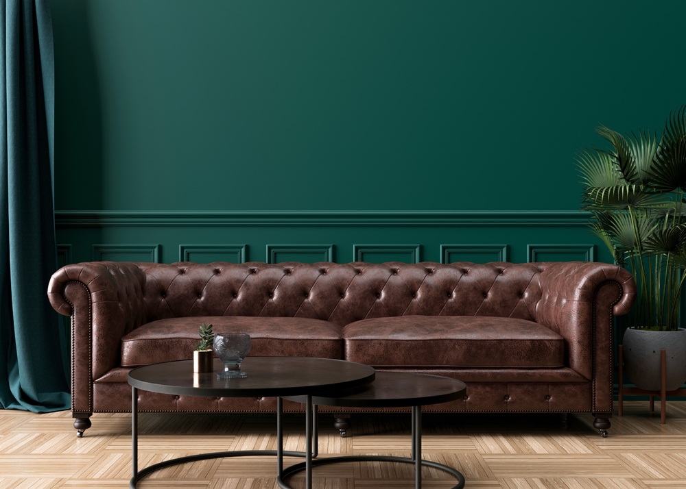 Empty green wall in modern living room. Mock up interior in classic style. Free space, copy space for your picture, text, or another design. Brown leather sofa, plant, parquet floor.